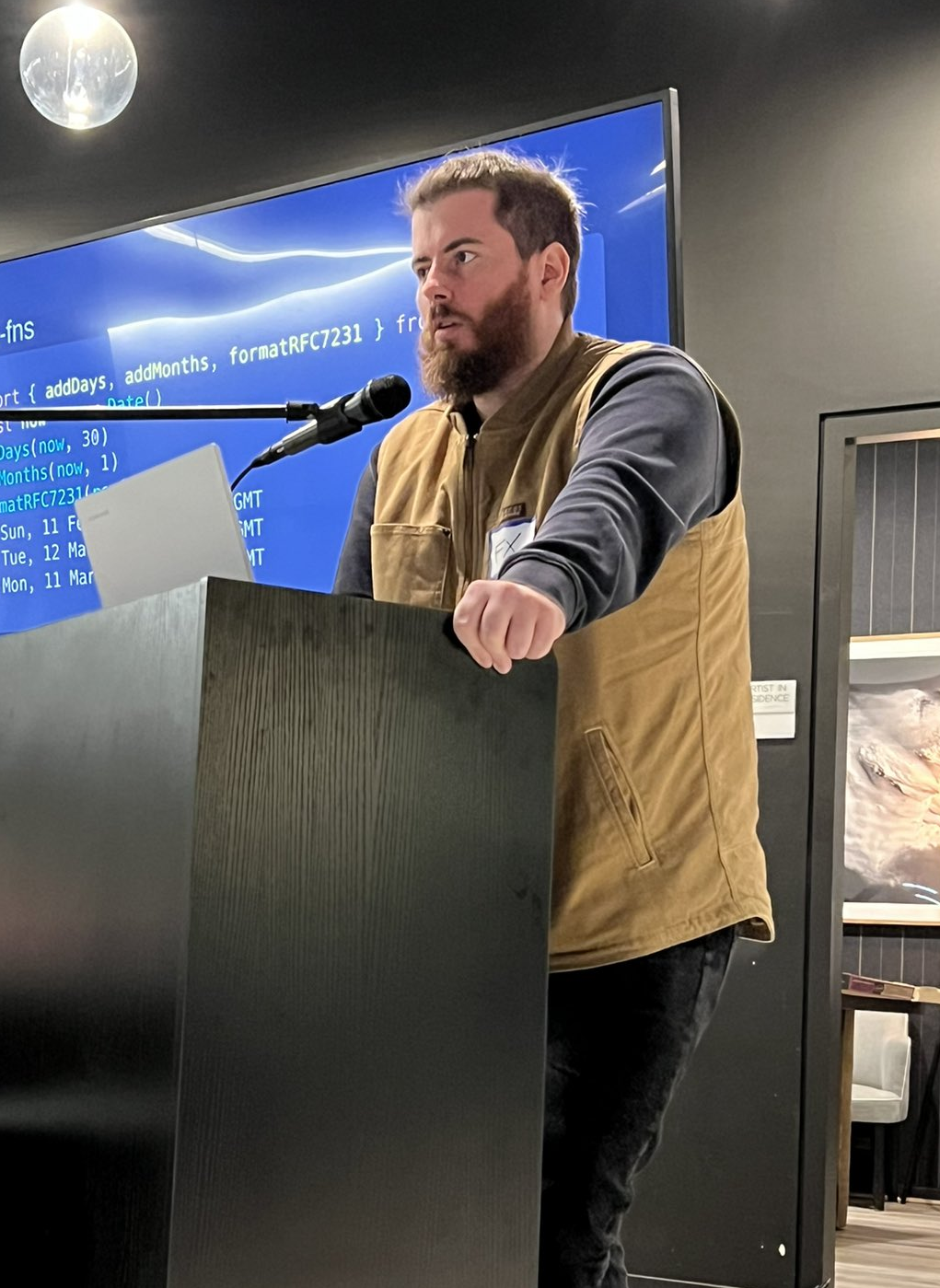 FX speaking in front of a TV, looks like a presentation
